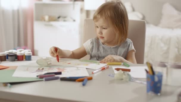 Linda niña se sienta a su mesa y dibuja con lápices de colores. Feliz con los resultados que sonría.Su habitación es de color rosa, dibujos bonitos colgando de las paredes, muchos juguetes por ahí . — Vídeo de stock