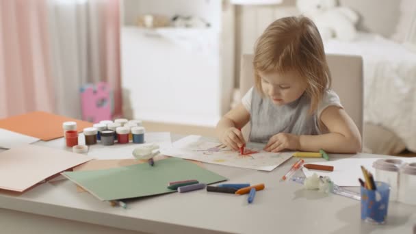 Nettes kleines Mädchen sitzt an ihrem Tisch und zeichnet mit Buntstiften. Ihr Zimmer ist rosa und gemütlich. — Stockvideo
