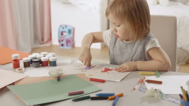 Nettes kleines Mädchen sitzt an ihrem Tisch und zeichnet mit Buntstiften. Ihr Zimmer ist rosa und gemütlich. — Stockvideo