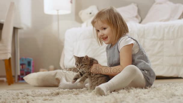Linda niña se sienta en el suelo y felizmente sostiene a su gatito a rayas favorito. Moción lenta . — Vídeo de stock