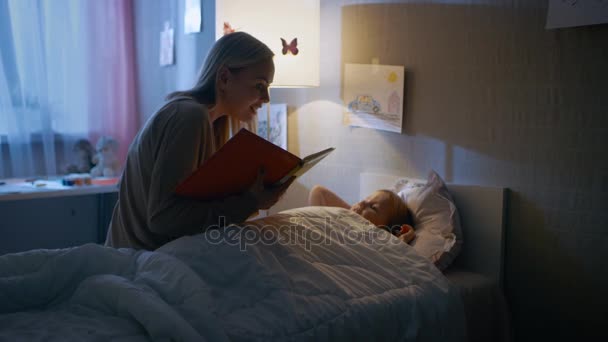 Mladí milující matka čte pohádky na její malou krásnou dceru, která jde do spánku, v její posteli. — Stock video