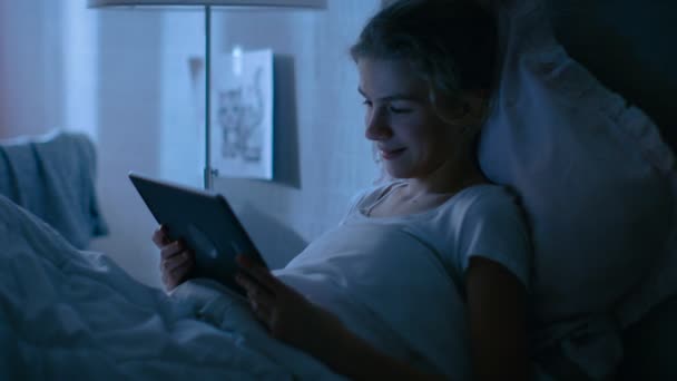 Jeune adolescente repose dans son lit la nuit avec tablette. Montres TV Show et Smiles . — Video