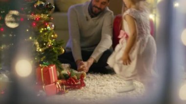 Karlı pencereden bakıyor. Mutlu baba, anne ve kızı Noel ağacın altında oturup. Kızın annesi için bir hediye verir.