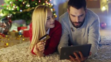 Mutlu çift yalan Noel ağacı, kadın tutar kredi kartı ve adam altında halı üzerinde satın hediyelerini Tablet bilgisayarda.