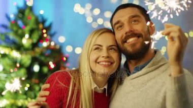 Mutlu çift ışık havai fişekleri ve gülümseme. Arka plan Christmas Tree ve ışıkları ile dekore edilmiş Oda.