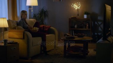 Oturma odasında onun kanepede oturan güzel ve genç birbayan. O patlamış mısır ve saatler televizyon yiyor. Bu akşam, oda rahat görünüyor.