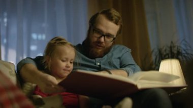 Akşamları, baba ve küçük kızı oturan bir kanepe oturma odası onlar okuma çocuk kitapları vardır.