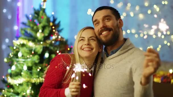 Glückliches Paar zündet Wunderkerzen an und lächelt. im Hintergrund Weihnachtsbaum und beleuchtetes Zimmer. — Stockvideo