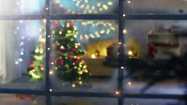 Szép mozgó lövés a havas utca az ablakba. Díszített karácsonyfa, ajándékok alatt vele, és sok-sok karácsonyi fények a teremben, meghitt ünnepi hangulatot látva.