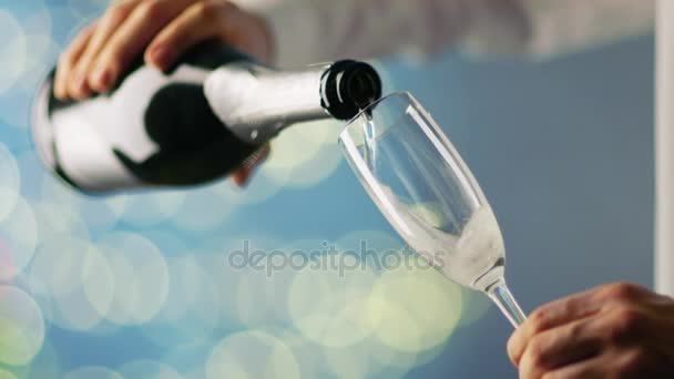 Hombre con camisa blanca vertiendo champán en la copa de champán. El fondo es azul con luces borrosas brillando . — Vídeos de Stock