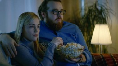 Erkek ve kız arkadaşı Tv izliyor. Onlar onların rahat oturma odasında kanepede oturup patlamış mısır yemek. Akşam oldu.