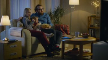 Bir baba, anne ve küçük kızı Tv izlerken düşük ihtimal. Onlar onların rahat oturma odasında kanepede oturup patlamış mısır yemek. Akşam oldu.