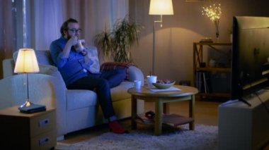 Akşam adam onun oturma odasında bir kanepede oturuyor. O gıda konteyner üzerinden Asya yemek yeme ve Tv programı izlerken.