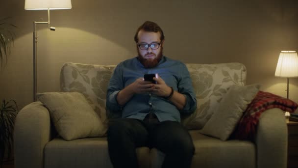 Człowiek siedzi na kanapie w salonie — Wideo stockowe