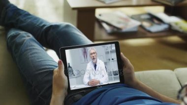 Kanepede yatan ve doktoru ile görüntülü konuşma bir Tablet bilgisayarda sahip hasta adamı.