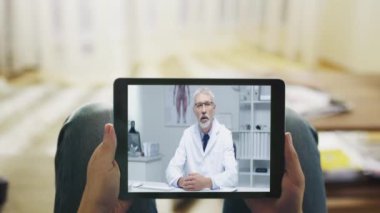 Hasta adam kanepede yatan ve doktoru ile görüntülü konuşma bir Tablet bilgisayarda sahip. Bakış açısı Shot.