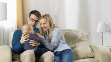 Oturma odası mutlu aile içinde bir kanepede oturan. Babanın Lap'ın hem baba ve anne sevgiyle kucaklamak üzerinde bebek oturur.