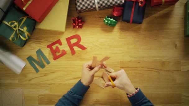 Zeitraffer eines Mannes, der Buchstaben für Wörter wie "Frohe Weihnachten" schneidet und sie mit Geschenkverpackungen auf den Holztisch legt. — Stockvideo