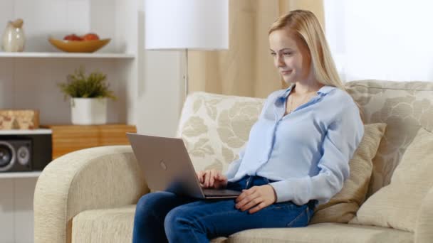 Giovane bella donna seduta nel suo salotto e al lavoro sul suo computer portatile . — Video Stock