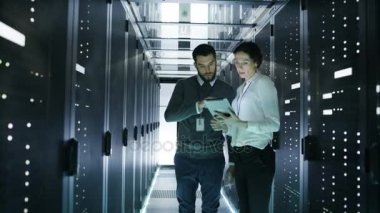 Erkek ve kadın sunucu teknisyenleri veri merkezinde çalışıyor. Çalışan Rack Server tanılama. Kadın kullanır Tablet bilgisayar.