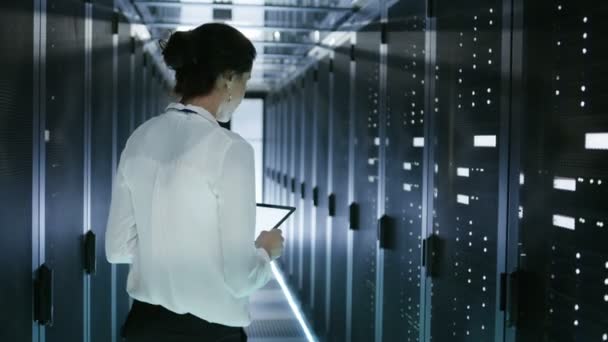 Female Server Technician Walking in Data Center Corridor with Rows of Rack Servers. She's Running Diagnostics on Her Tablet Computer — Stock Video