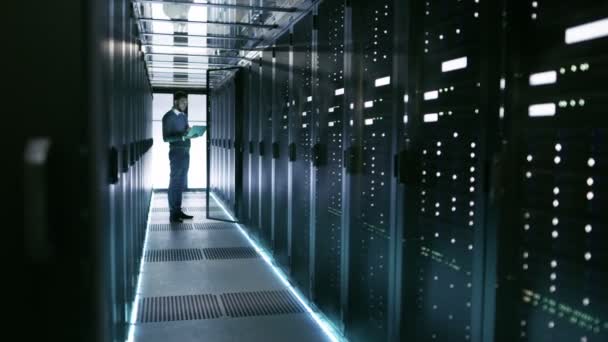 Ingénieur serveur masculin dans le centre de données. Il se tient devant la porte ouverte du serveur de rack et travaille sur son ordinateur portable .