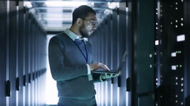 Erkek bu açık Server raf kabine büyük veri merkezindeki önce ayakta bir dizüstü bilgisayar üzerinde çalışan teknisyeni.