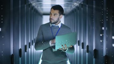 Erkek mühendisi büyük bir veri merkezinde bulunan bir dizüstü bilgisayarda çalışır. Raf tipi sunucular satırlarının görülür.