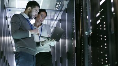 Erkek ve dişi Server mühendisleri iş veri merkezindeki bir dizüstü bilgisayarda. O sunucu kabine açılır.