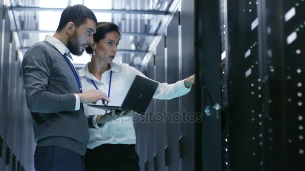 Homme IT Specialist détient ordinateur portable et discute de travail avec une technicienne serveur. Ils sont debout dans le centre de données, Rack Server Cabinet est ouvert .