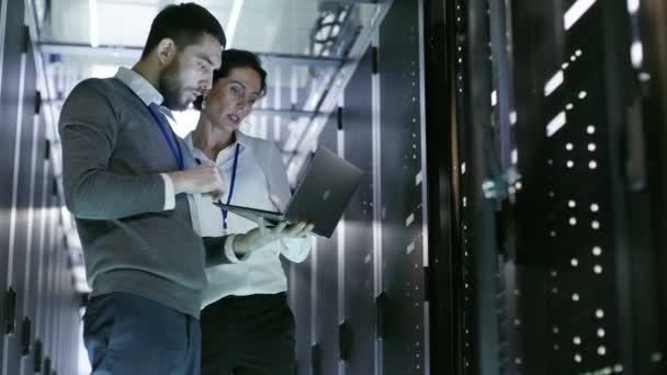 Инженеры мужского и женского пола работают над ноутбуком в центре обработки данных. Он открывает серверный кабинет . — стоковое видео