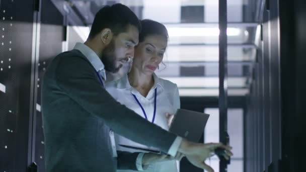 Ingenieros de servidores masculinos y femeninos trabajan en una computadora portátil en el centro de datos. Abre el gabinete del servidor Rack . — Vídeos de Stock