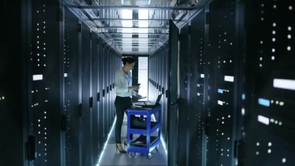 Ingeniera de TI femenina trabaja en un ordenador portátil y escanea los discos duros que se encuentran en un carro. Trabaja en Data Center . — Vídeos de Stock