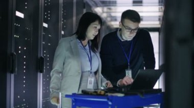 Beyaz erkek ve Asya kadın o teknisyenleri çalışma büyük veri merkezi raf tipi sunucular tam Crash Cart dizüstü bilgisayar ile.