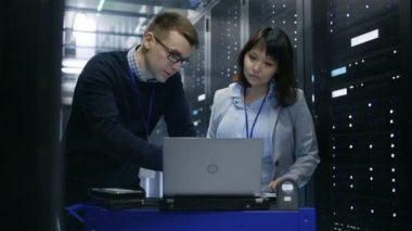 Erkek bu uzman bir dizüstü bilgisayarda kadın Server teknisyen için bilgileri gösterir. Veri merkezinde duruyorlar.