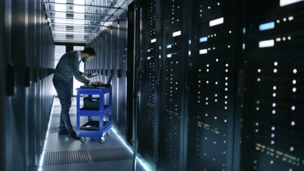 IT Engineer travaille sur un ordinateur portable et scanne les disques durs qui reposent sur un chariot d'accident. Il travaille dans le centre de données .