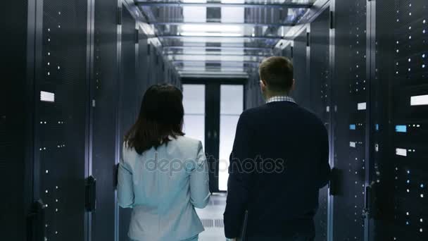 Back View of Male and Female IT Engineers Walking in Data Center with Rows of Rack Servers. They Have Discussion, She Holds Tablet Computer. — Stock Video