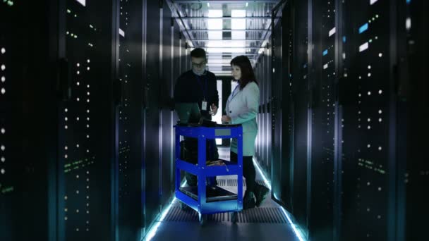 Kaukasische Serveringenieurinnen und Serveringenieurinnen arbeiten mit Crash-Cart-Laptop in großem Rechenzentrum voller Rack-Server. — Stockvideo