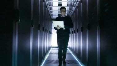 Erkek sunucu mühendis raf tipi sunucular satırlar arasında açık dizüstü bilgisayar ile yürür. O büyük, fütüristik veri merkezinde çalışıyor.