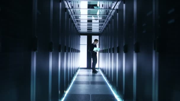 Αρσενικό το μηχανικός εργάζεται σε ένα φορητό υπολογιστή σε ένα μεγάλο κέντρο δεδομένων. Σειρές των διακομιστών για Rack έχουν δει. — Αρχείο Βίντεο