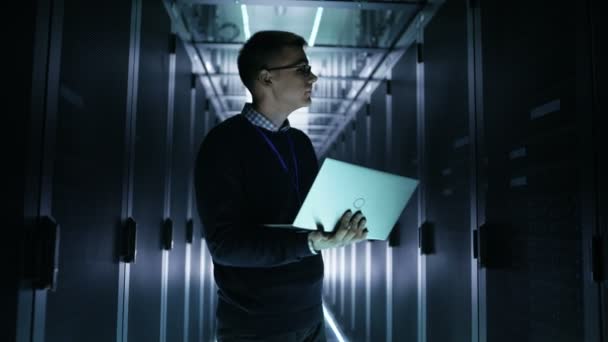 Plan médian de l'ingénieur serveur lisant les données du serveur rack et l'analysant sur un ordinateur portable. Il travaille dans un centre de données avec des rangées de serveurs de rack . — Video