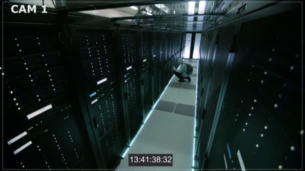 Cámara de seguridad N1 Filmación de un hacker con capucha en el centro de datos, con su computadora portátil se conecta a uno de los servidores de rack, comete delitos y deja . — Vídeo de stock