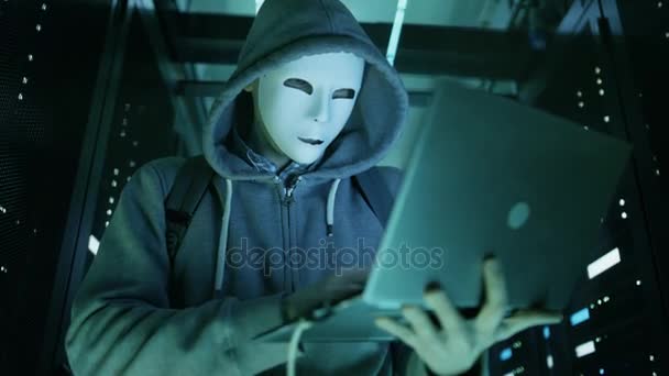 Mitten av skott av en maskerad Hacker i hålla Laptop och Hacking dataserver. — Stockvideo