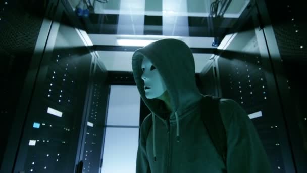 Gemaskerde Hacker in een Hoodie doorloopt Corporate Data Center met rijen rackservers te werken. — Stockvideo