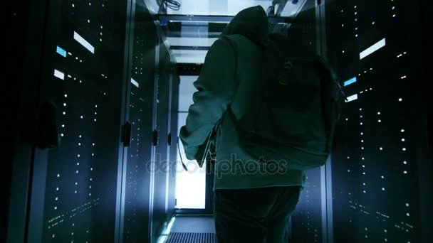 Χαμηλή γωνία πυροβολισμό του έναν μασκοφόρο χάκερ στο ένα Hoodie κρυφός μέσα από το εταιρικό κέντρο δεδομένων με τις σειρές των διακομιστών για Rack. — Αρχείο Βίντεο
