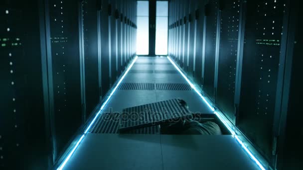 Hacker à capuchon dans un masque grimpe sous le plancher Hatch dans le centre de données. Il se connecte à l'un des serveurs Rack avec son ordinateur portable .