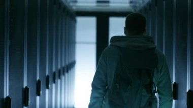 Onun Hoodie ve yürüyüş yoluyla veri merkezi koridor üzerinde bir Hacker koyma arkadan görünüm, 