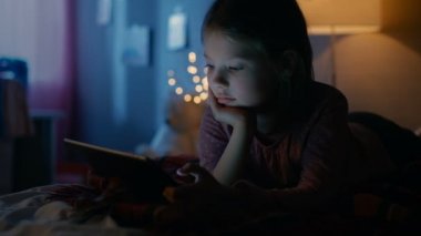 Sevimli küçük kız onun odasına gece, Tablet bilgisayar ile bir yatakta yatıyor. Açık onun gece lambası.