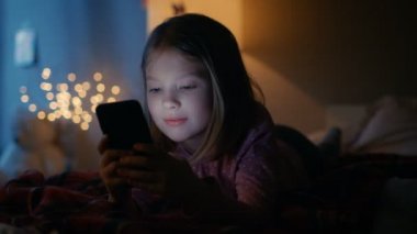 Onun odasına gece, sevimli küçük kız yatak kullanır Smartphone'da yatıyor. Açık onun gece lambası.
