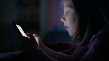 Onun odasına gece, sevimli küçük kız yatak kullanır Smartphone'da yatıyor. Ekran yüzü yanar.